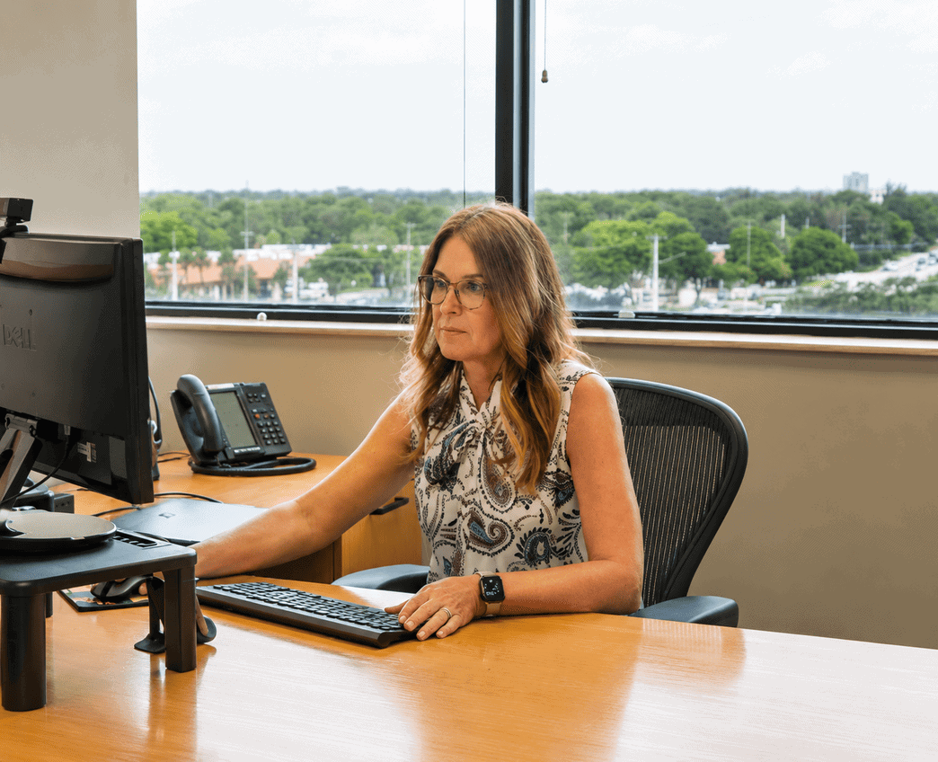 Professional woman working at her desk in an office with a view of the city and greenery outside.