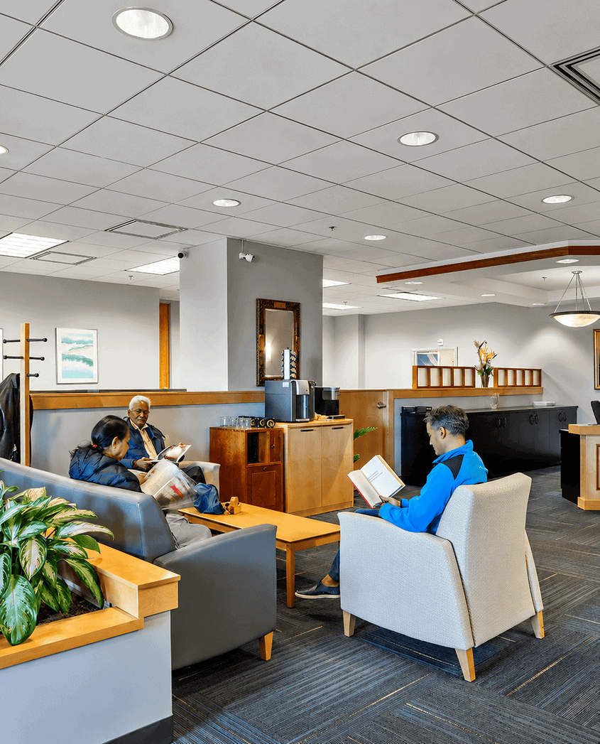 Business professionals waiting in a modern office lounge area with comfortable seating and reading materials.